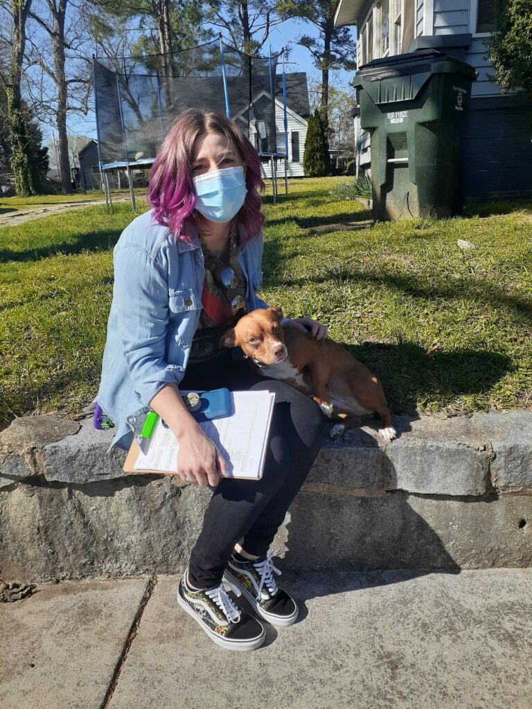 Woman sits with dog on sidewalk with a clipboard