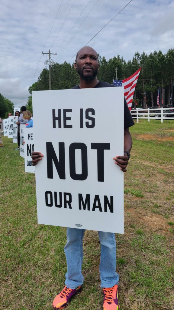 Man holding sign reading "He is not our man"