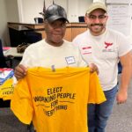 Two people smiling and holding a shirt that reads "Elect Working People for Everything"